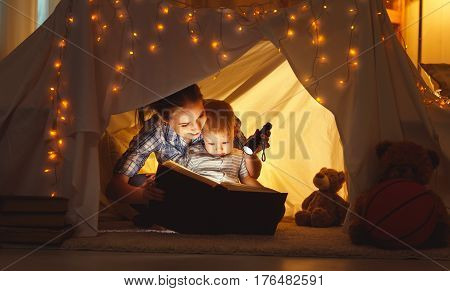reading and family games in children's tent. mother and child daughter with book and flashlight before going to bed