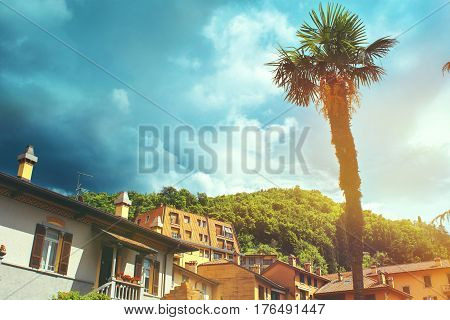 Beautiful toned cityscape of italian Varenna city with building big palm green valleys and dramatic sky before the rain