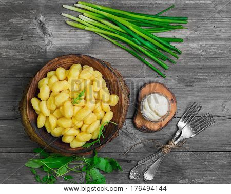 Homemade Potato dumplings Gnocchi in wooden plate. On gray wooden table background ingredients for Potato dumplings Gnocchi Salad of rucola fresh green onion sauce forks.