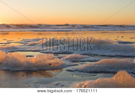 Sea foam at sunset on a beach.