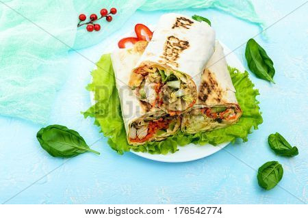Shawarma - Middle Eastern dish made from lavash (pita) stuffed with chicken mushrooms fresh vegetable salad sauce. Serving on lettuce leaves on a light background. The top view.