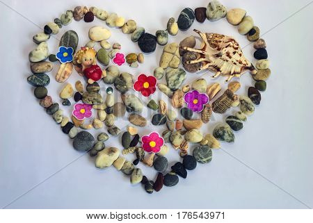 On a white background sea stones are laid out in the form of a heart and a large shell among them an angel with a red heart in his hands and the inscription 