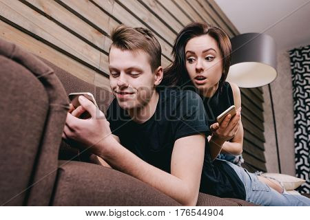 young couple lying in bed. One of them use the phone and flirting. other person is jealous and spies. concept of jealousy and distrust.
