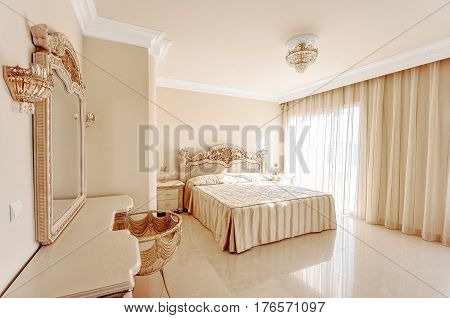 Luxurious bedroom in pastel colours in a neoclassical style with a large bed and a dressing table with marble floors.