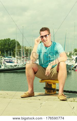 Summertime vacation adventure concept. Man spending his free time walking on marina sightseeing during summer guy sitting on bitt.
