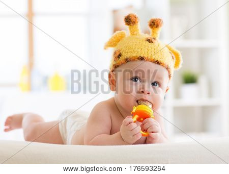Funny baby boy in giraffe hat lying on his belly in nursery. Little kid infant using nibbler.