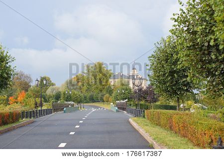 Road with markings to a beautiful old building through the autumn well-tended park.