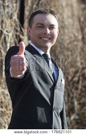 Young businessman smiling and showing thumbs up