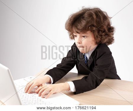 Cute little businessman typing on a laptop. Gray background.