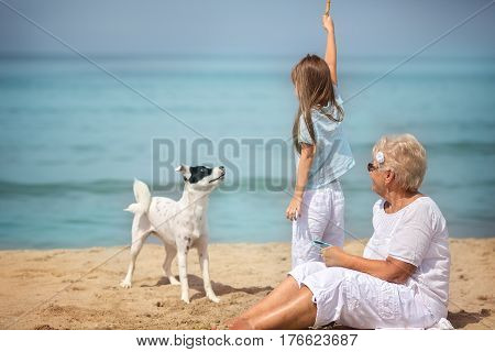 Happy grandmother has fun with granddaughter and her pet on the seaside