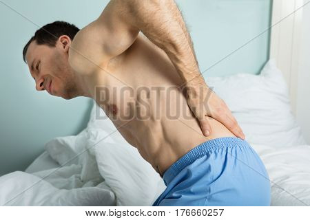 Close-up Of A Man Sitting On Bed Suffering From A Back Pain At Home