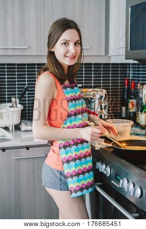 Portrait of young Caucasian woman girl with long hair cooking food pancakes standing in kitchen indoors at home authentic real people lifestyle