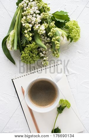 Feminine flatlay with spring flowers and ccoffee on white textured tabletop