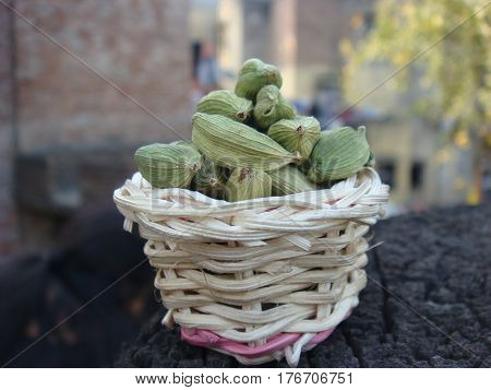 Green cardamom in small bamboo basket on rusted wooden stack