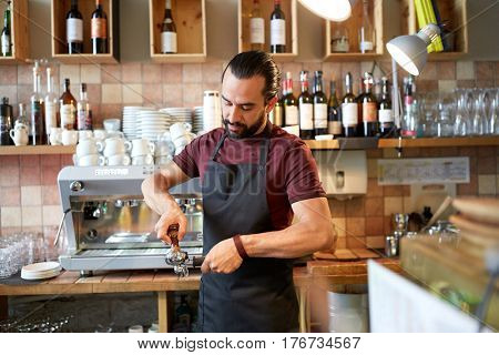 small business, people and service concept - man or waiter in apron with holder and tamper preparing espresso at coffee shop