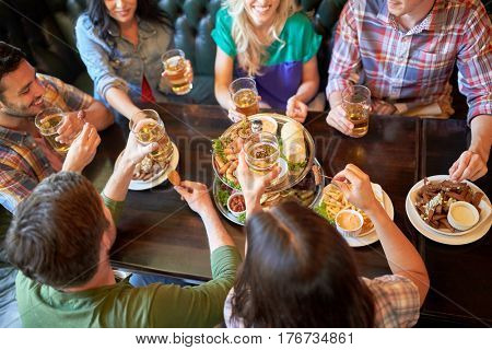 leisure, food, drinks, people and holidays concept - happy friends eating snack and drinking beer at bar or pub