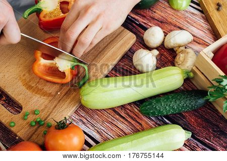 Cook cuts peppers on a wooden board. Cutting different vegetables on a wooden board. Tomatoes zucchini cucumber mushrooms