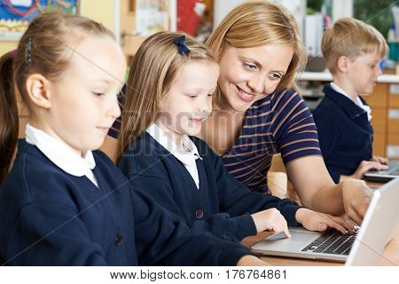 Teacher Helping Female Elementary School Pupils In Computer Class