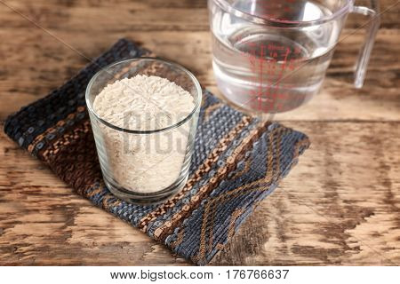 Glass of rice and measuring jug with water on wooden table