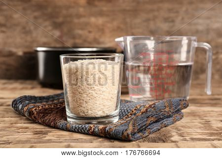Glass of rice and measuring jug with water on wooden table