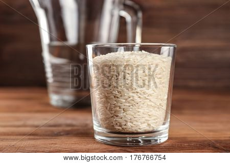 Glass of rice and measuring jug with water on wooden table