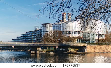 STRASBOURG FRANCE - DEC 25 2015: View through trees of the European Court of Human Rights building in Strasbourg France on a warm winter day and Ill river. ECHR is a international court established by the European Convention on Human Rights.
