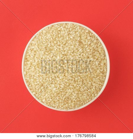 Raw medium grain rice in a bowl on red background. Gluten free grain