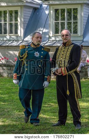 Saint Petersburg, Russia - may 15, 2016: Actors demonstrate vintage clothing 19 century in the Park. Two older men in old uniforms pose in front of green meadows and facade of the old house
