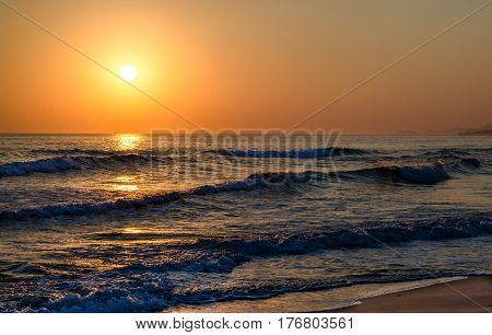 Sunrise over the sea, the rolling calm waves, sandy beach. Skay orange, waves blue.