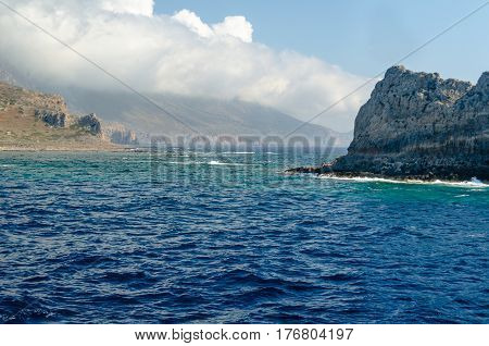 The rocky coast of the Mediterranean sea against the blue sky and clouds.