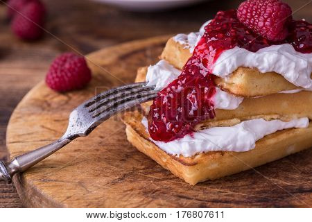 Belgian waffles with raspberries and double cream on rustic table.