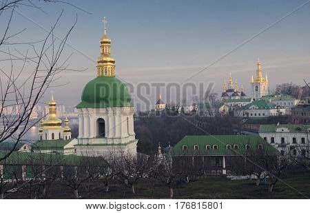 The green dome of the bell tower with the golden cross on the territory of the Kiev-Pechersk Lavra against the blue sky