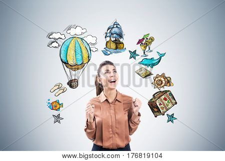 Portrait of a happy businesswoman in brown screaming with joy near a gray wll with travel sketches drawn on it.
