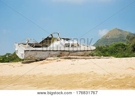 Broken yacht on the seashore. Old white boat on the sand near the sea or the ocean