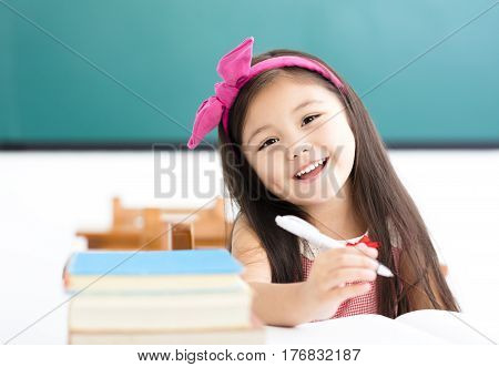 happy little girl writing at desk in classroom