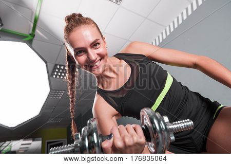 Young confident woman doing biceps curl exercise with dumbbells in fitness center. Slim girl training in the gym with dumbbells