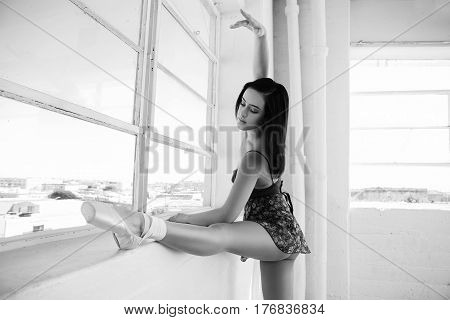 Beautiful ballerina stretches herself near the window in a dancing studio