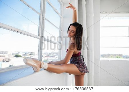 Ballerina stretches herself near the window in a dancing studio