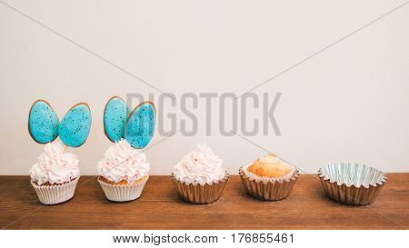 Delicious cupcakes with white cream and blue cakepops in row placed on wooden surface. White background with copyspace for text. Concept of creating sweets. Baking and cake decorating timeline
