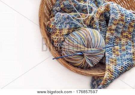 Knitting a scarf from a multi-colored six on a white background. Multicolored pattern, warm, cozy. Knitting at the wicker basket.