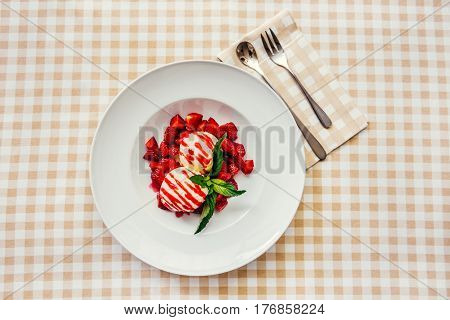 Strawberry ice cream dish with fresh strawberry and green petal serve on decorated with checkered cloth table