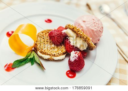 Strawberry ice cream dish with fresh strawberry, fresh cookie and green petal serve on decorated with checkered cloth table
