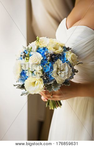 Bride holding delicate and tender marriage bouquet of yellow roses and other flowers, with green petals