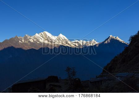 Bright Day Mountain View in Nepalese Himalaya with remote snowy peaks highlighted by rising sun while deep valley still in shadow