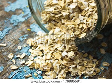 raw oatmeal is scattered on the desk of the bank in which the oat flakes are stored. blue background in the style of Shabby Chic. white spoon with uncooked oatmeal