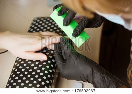 Top view manicurist polishing index finger for manicure in nail beauty salon. Step of manicure process.
