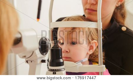 Child's healthcare - little girl with mother in ophthalmological clinic checks eyesight, telephoto