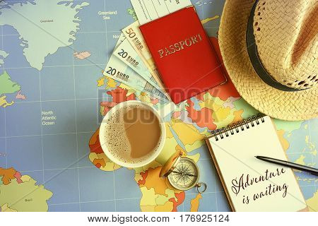 Text ADVENTURE IS WAITING written in notebook and travel stuff on world map background