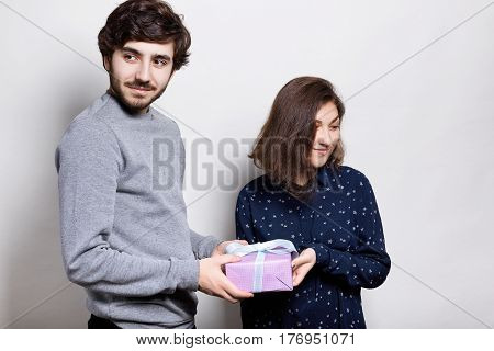 A happy couple with present. A hipster guy presenting a gift to his girlfriend looking aside. Young male and female isolated over white background. People and relationship concept.