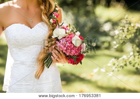 Bride holding delicate and tender marriage bouquet in white and pink colours with green petals. Beautiful sunny day in park.